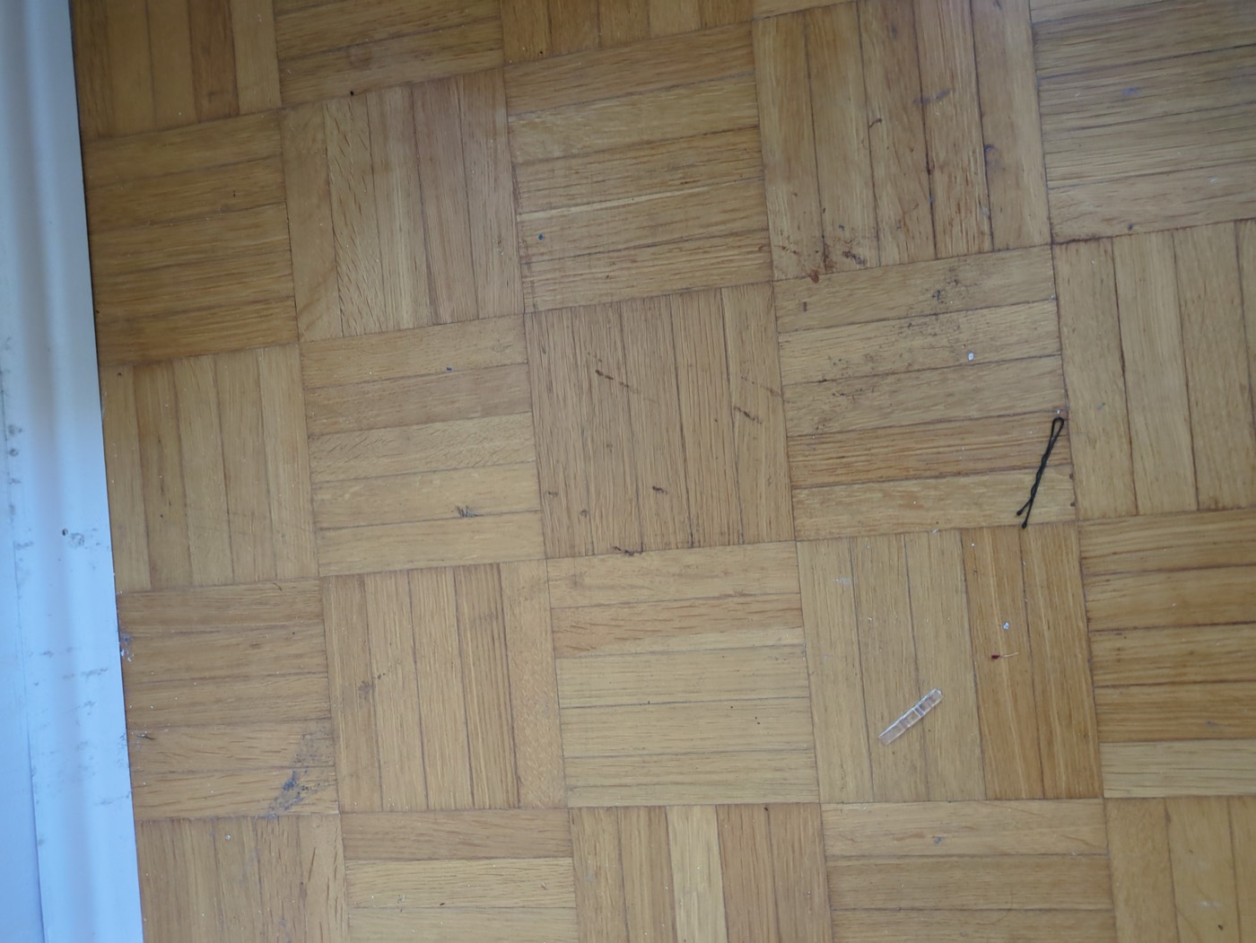 Parquet with scratches, dark marks and scuffed blocks near the skirting